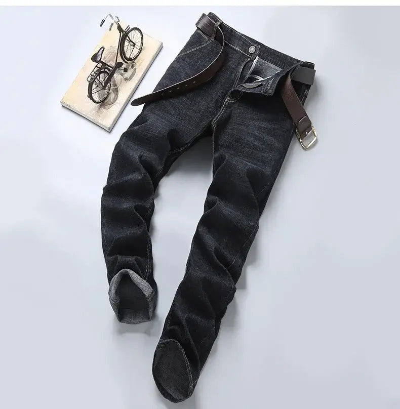 Jeans en denim extensible à coupe slim pour hommes en lavage foncé, avec des bas retroussés et une ceinture en cuir marron passée dans les passants.