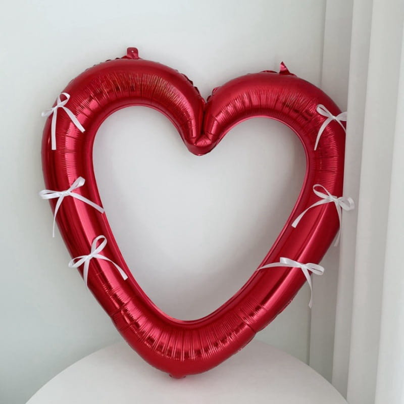 Un globo de lámina con corazón rojo brillante para marco de foto de 40 pulgadas, adornado con pequeños moños blancos a lo largo de sus bordes.