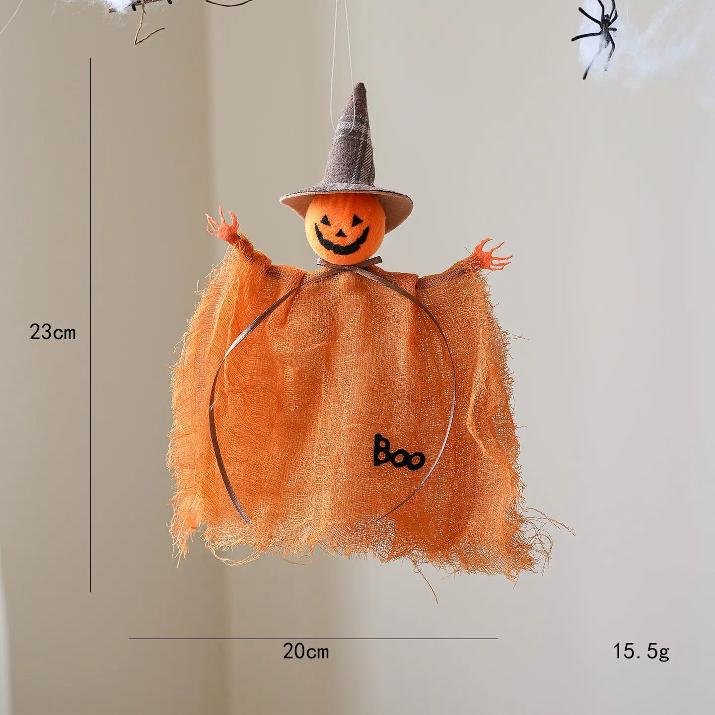 Figura colgante de tela de adorno de halloween de bruja colgante naranja con un ornamento de espantapájaros, con una carita sonriente cosida, lleva un sombrero de bruja de cuadros grises y tela deshilachada con la palabra boo bordada en su pecho.