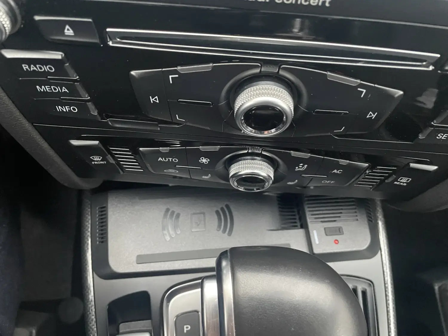 Soporte de cargador inalámbrico para Audi A4 Q5 de 15 W instalado en el panel negro del sistema de audio y control de climatización del automóvil, con perillas giratorias plateadas.