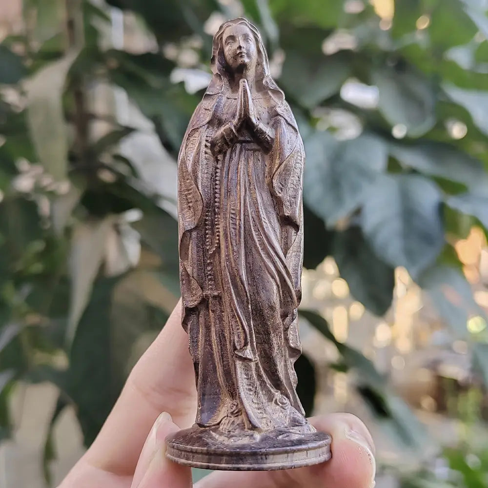 Statuette de la Vierge Marie en bois sculpté à la main, représentant une statue détaillée de couleur bronze, tenant un chapelet et se tenant en posture de prière.