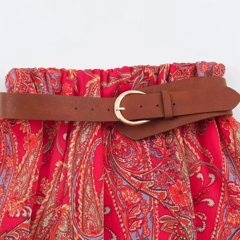 brown leather belt with a gold toned buckle worn around the waist of a red paisley patterned midi skirt in the red paisley halter top and midi skirt set