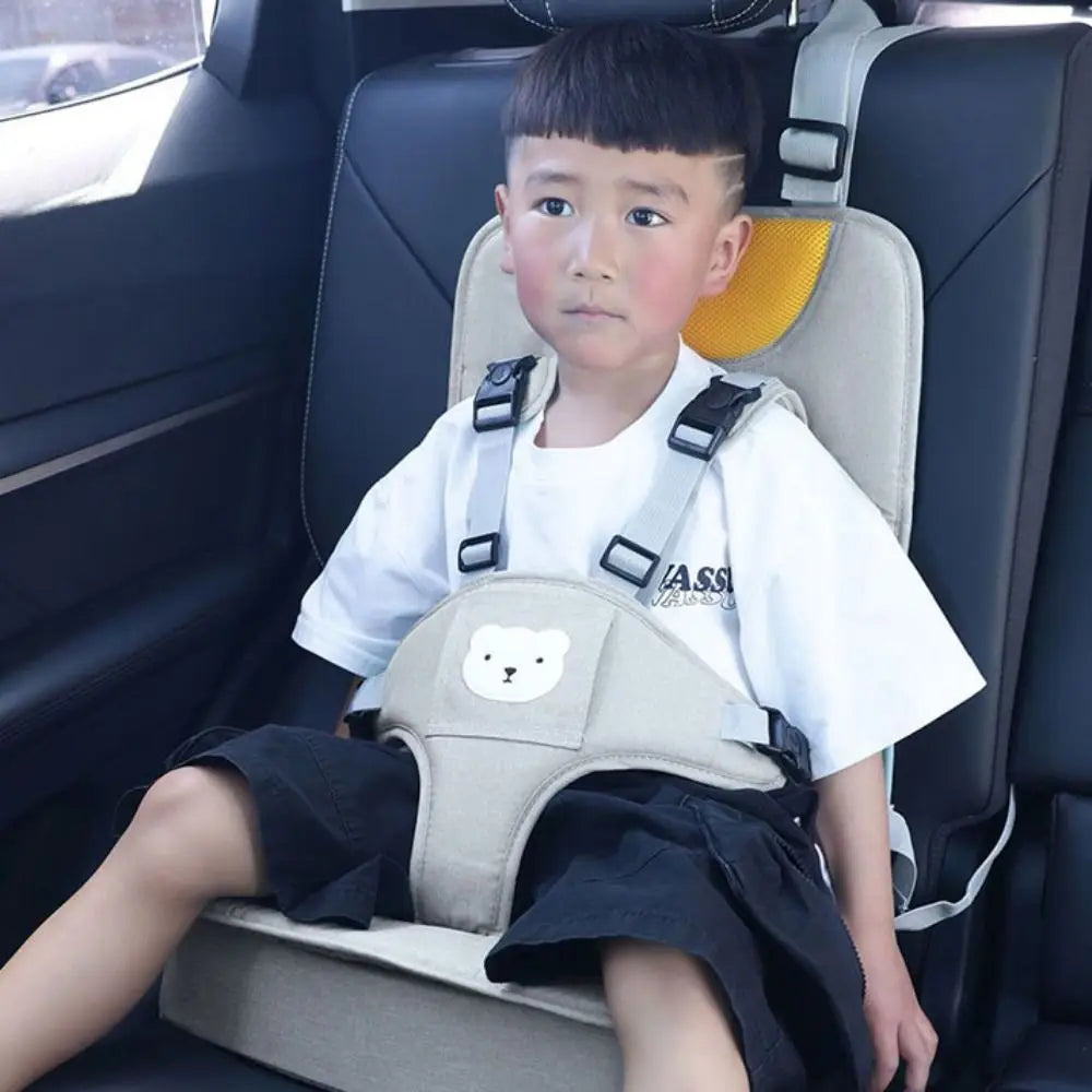 Beiges Baby-Autokindersitzerhöhungskissen mit einem Sicherheitsgurt für Kleinkinder, schwarzen verstellbaren Trägern und einem weißen Bärengesicht-Patch.