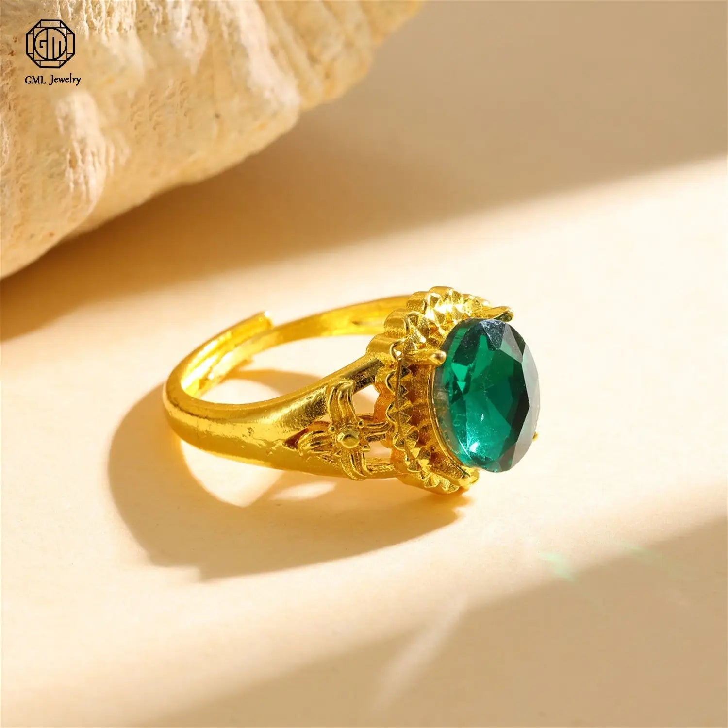 A sand gold adjustable ring featuring a matte wide band with an ornate filigree design and a prominent oval-cut emerald gemstone, crafted to be fade resistant.