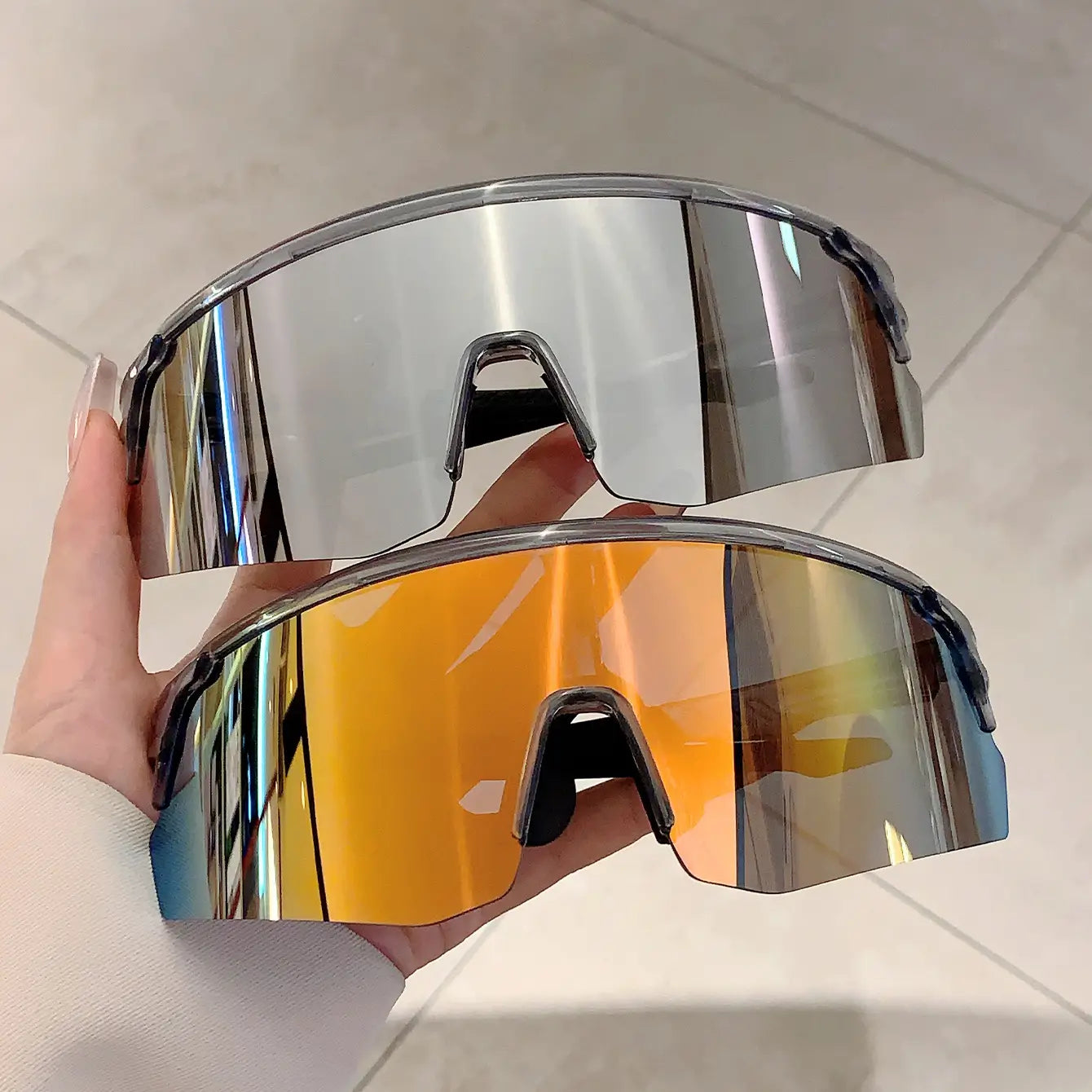 Une paire de lunettes de soleil de sport surdimensionnées, avec des verres réfléchissants miroir élégants en tons argentés et dégradé orange, conçues comme lunettes de cyclisme.
