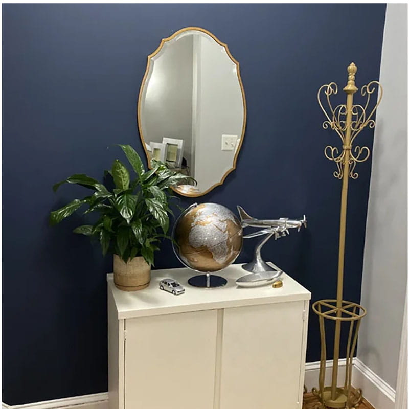 Un globe métallique avec une finition argent et or, présenté sur un meuble blanc, complète le style de décoration murale ovale dorée et ornementale des miroirs de salle de bains.