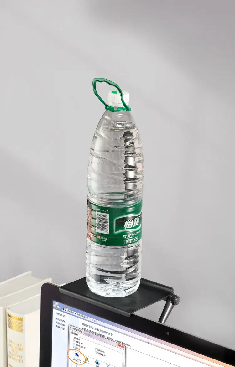 clear plastic water bottle with green cap and handle featuring a green label with white characters placed on an adjustable screen top storage shelf monitor stand.