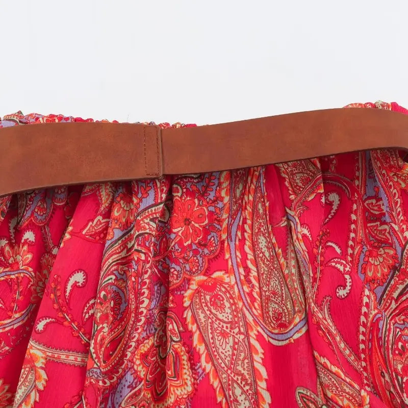 a vibrant red paisley midi skirt with a detailed pattern in shades of orange purple and cream, accented by a brown leather belt at the waist in the red paisley halter top and midi skirt set