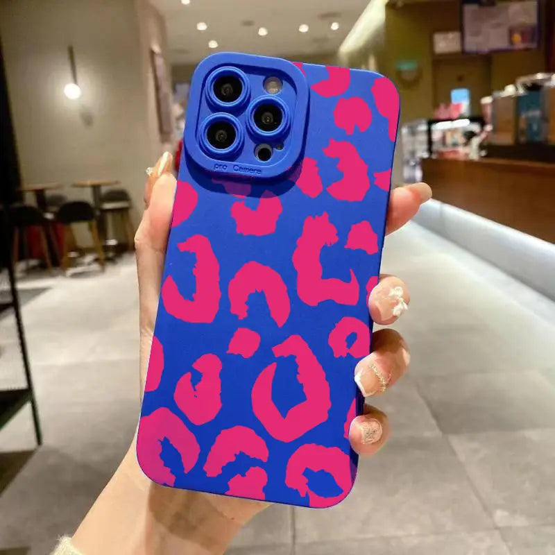 Image of the back side of a vibrant blue iPhone case with bold pink leopard print pattern and matching camera bump featuring a matte black leopard camera protective design.