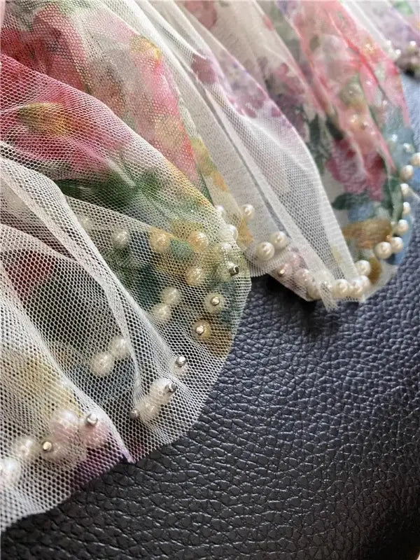 Una falda de tul translúcido con estampado floral delicado, con ribete de perlas, que presenta pequeñas perlas redondas y cuentas metálicas a lo largo del borde, diseñada en un estilo fairycore Y2k.