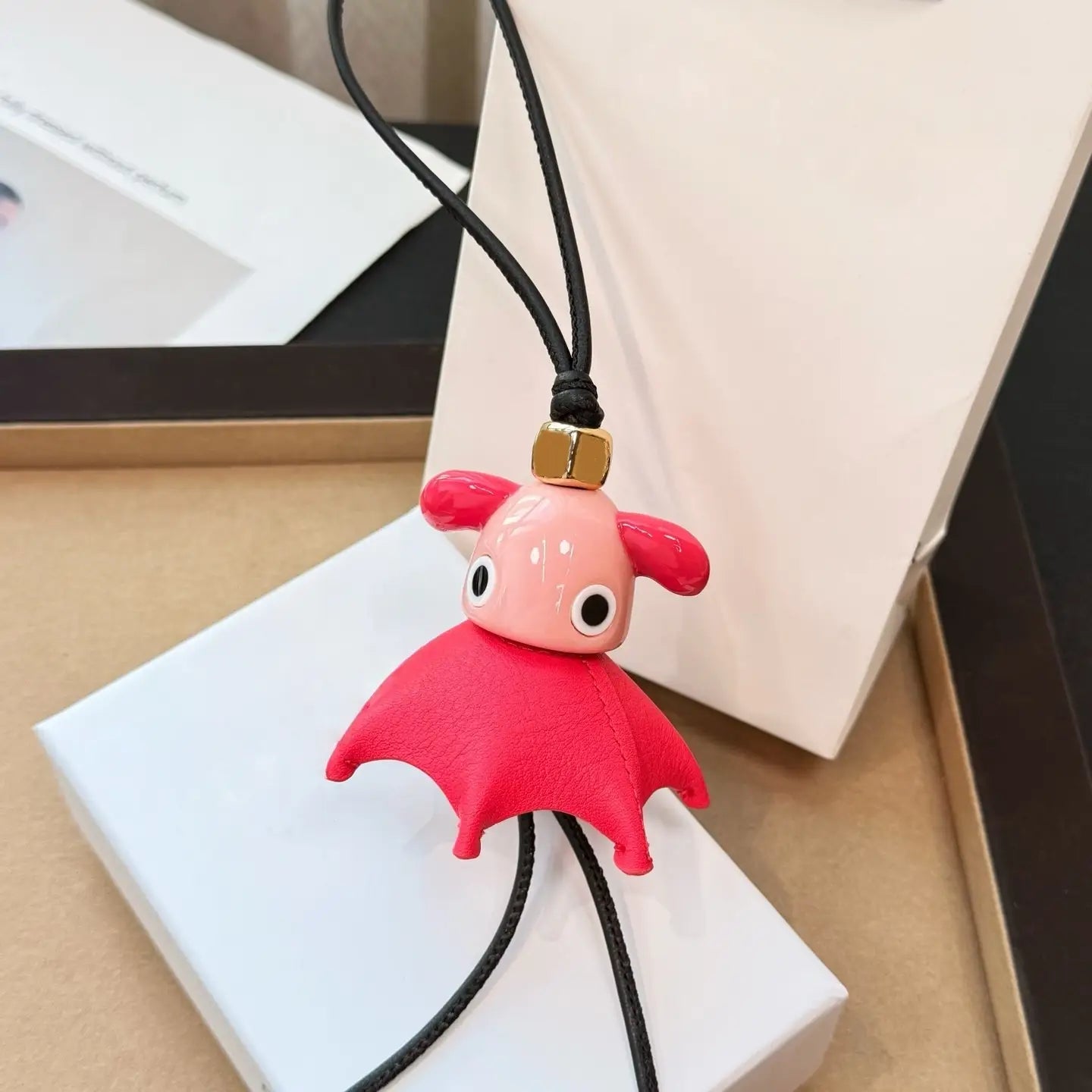 Llavero colgante para bolso con encanto de animales de cuero, tierno, de diseñador, con un llavero con forma de murciélago rosa, cabeza brillante y alas rojas con textura, sujetos a un cordón negro con un broche de acabado en tono dorado.