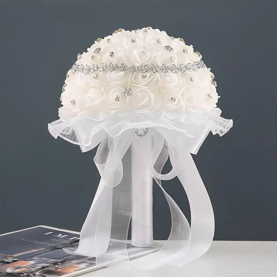 A delicate white bridal bouquet with satin roses adorned with sparkling rhinestones along a silver beaded band and flowing sheer ribbon ties.