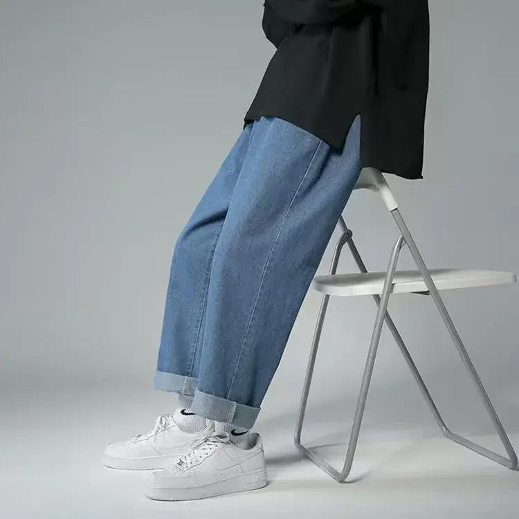 Jeans en denim bleu délavé clair avec broderie croisée, présentant des jambes amples et des revers retroussés.