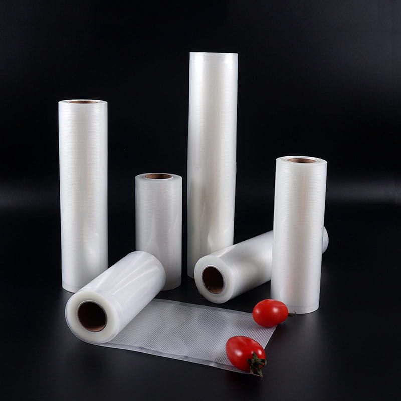 clear plastic food vacuum sealer rolls in varying sizes displayed on a dark surface with two cherry tomatoes, designed for food storage and preservation.