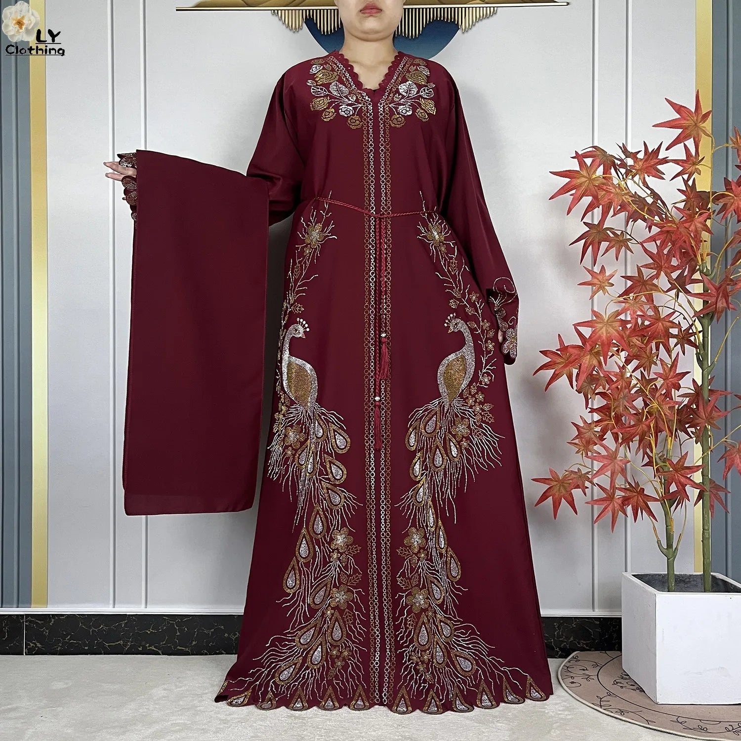 Ein bordeauxrotes Chiffon-Abaya mit Stickerei im islamischen Maxikleid-Stil, mit aufwendigen Pfauendesigns in Gold und Silber entlang der Vorderseite und der Ärmel.