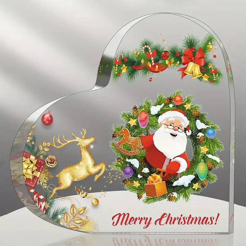 Adorno de escritorio navideño en forma de corazón de acrílico transparente, con un diseño festivo que muestra a Papá Noel con traje rojo, rodeado por una corona verde y renos dorados.
