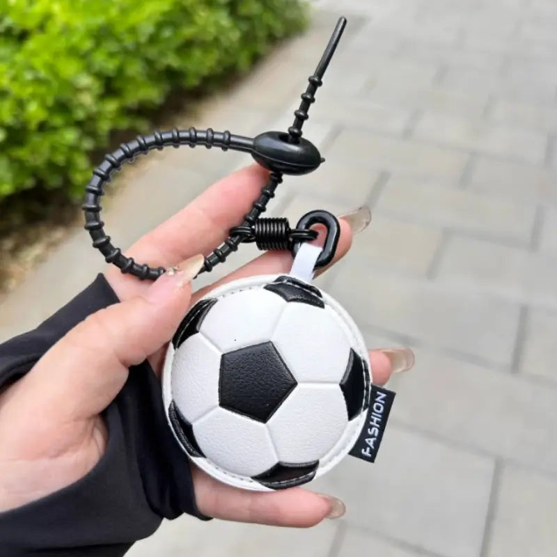 A black and white leather soccer ball keychain with a textured surface featuring a coiled strap and spring mechanism used as a bag charm.