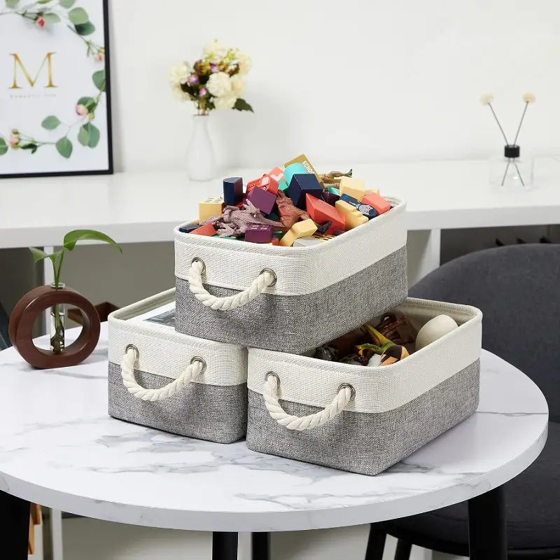 paniers de rangement en tissu pliables empilés gris et blanc avec texture tissée et poignées en corde pour un rangement organisé.