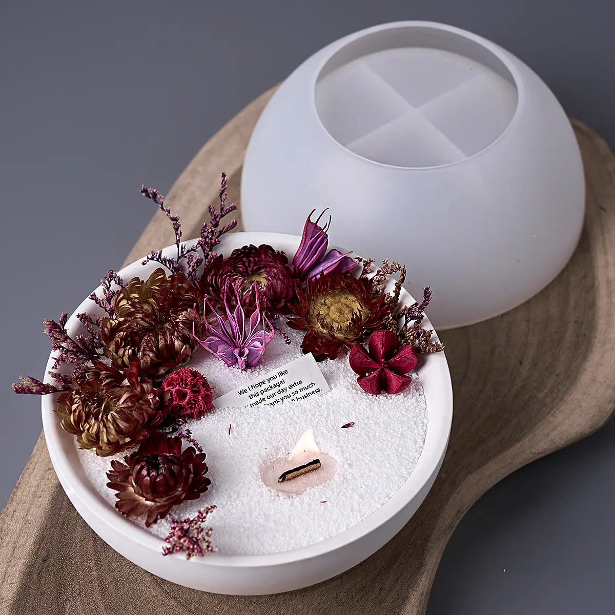 round silicone mold for concrete storage bowls and candles featuring a white ceramic candle holder with dried flowers and sand.