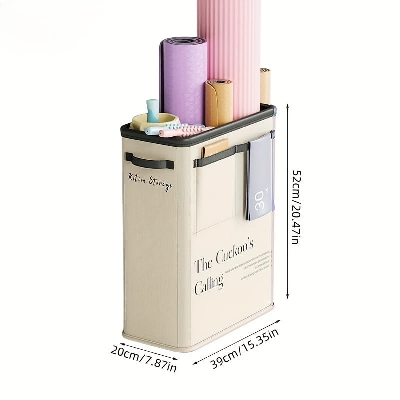 Beige fabric yoga mat storage basket with black trim and handles featuring printed text kitiv storage and the cuckoos calling designed to hold rolled yoga mats and accessories.