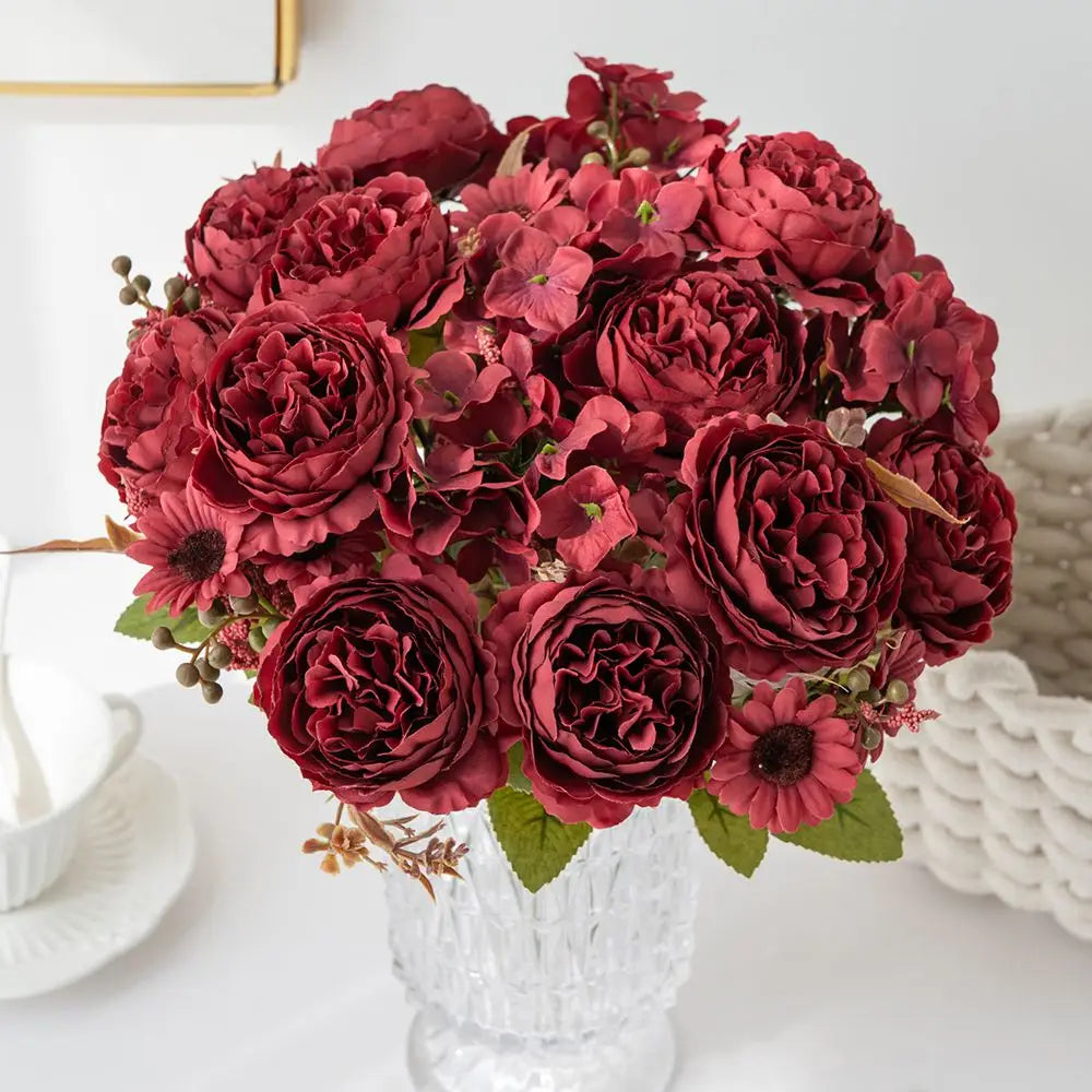 ein üppiges Arrangement aus tiefburgunderfarbenen künstlichen Blumen mit Rosen und Hortensien, in einer klaren, strukturierten Glasvase für die Wohnraumdekoration präsentiert