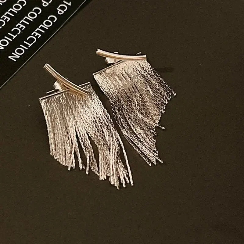 Boucles d’oreilles déclaration à frange en or avec bordure effet argent, composées d’un design minimaliste pendante, d’une finition métallique élégante et de détails délicats de frange.