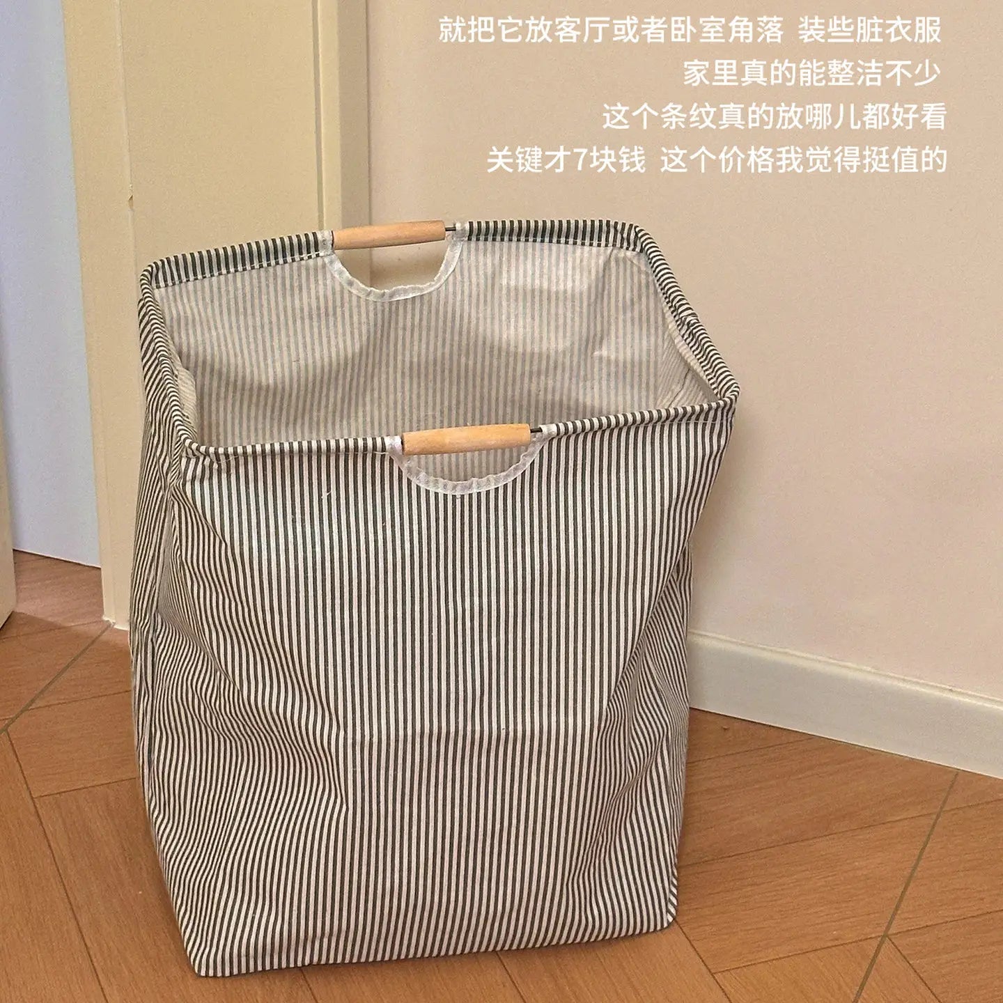 Ein gestreifter zusammenklappbarer Wäschekorb aus Canvas für Schmutzwäsche mit Holzgriffen und klarer Kunststoffverkleidung, entworfen zur Organisation von Schmutzwäsche.