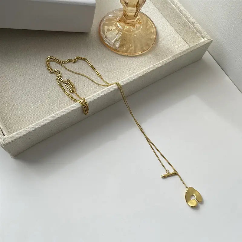 Collier pendentif à superposition géométrique doré délicat pour femmes, présentant une chaînette fine et deux pendentifs géométriques abstraits en forme de feuille de tailles variées.