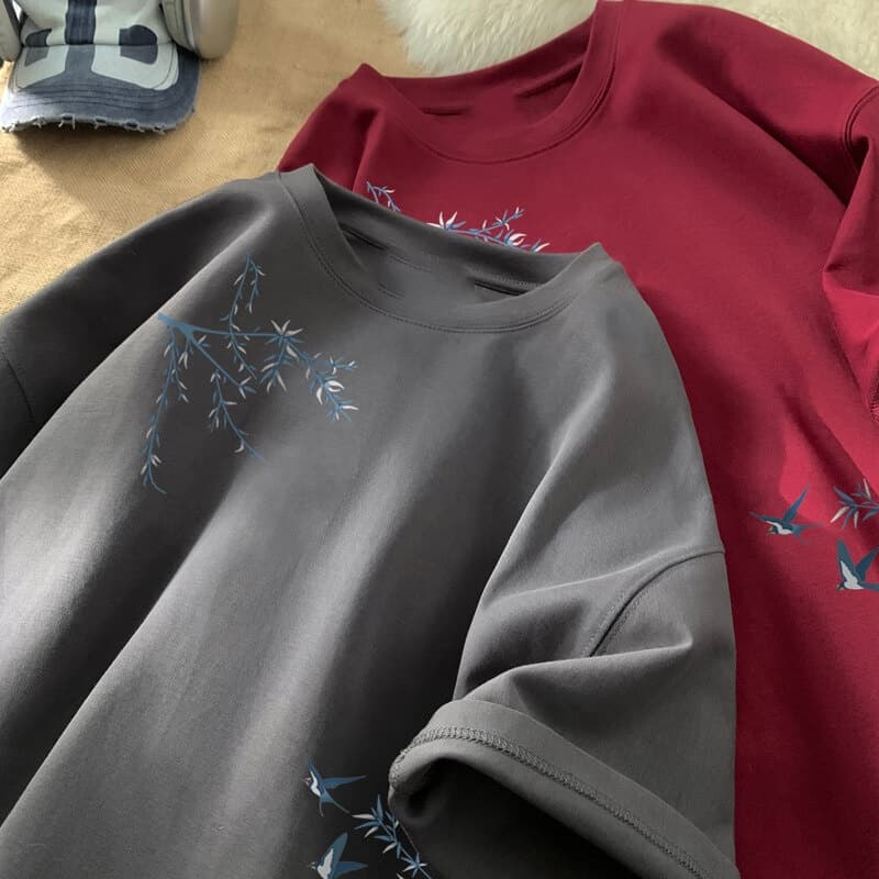 Camiseta de algodón oversize gris con delicadas ramas bordadas en azul y pájaros en la parte delantera.