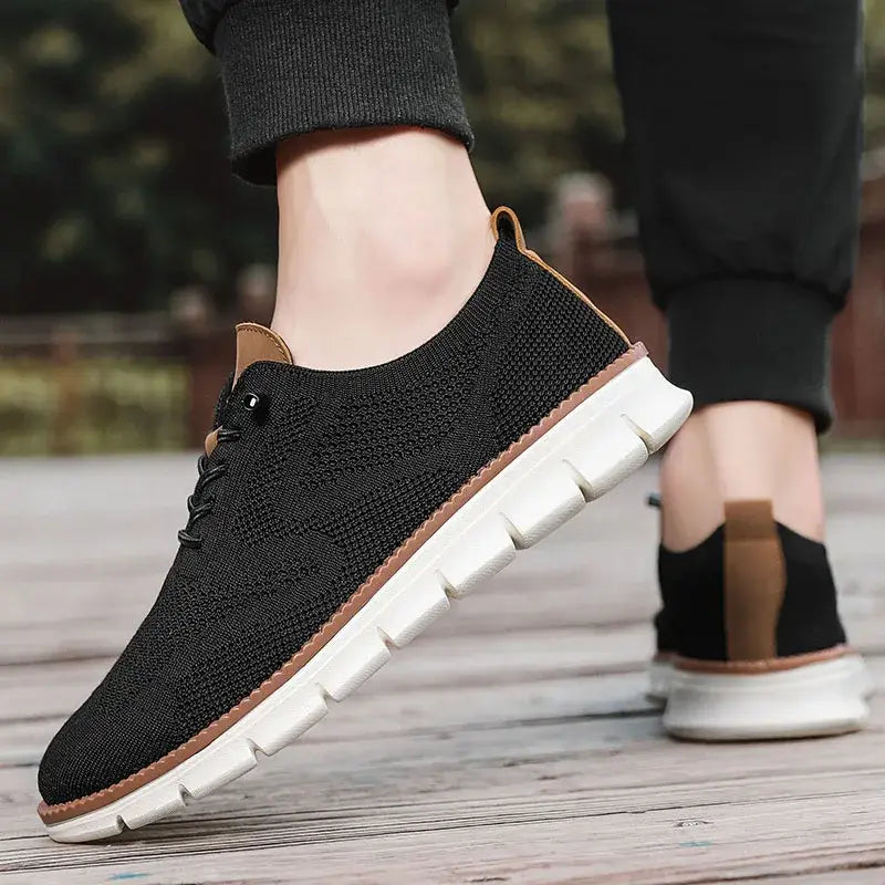 Chaussures derby brogue décontractées en maille pour hommes, de couleur noire, avec des semelles blanches et des accents tan, fabriquées à partir d’un matériau en maille.