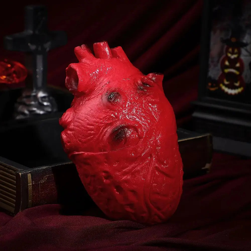 a glossy red fake bloody human heart halloween prop with an anatomically detailed textured surface and darkened indentations.