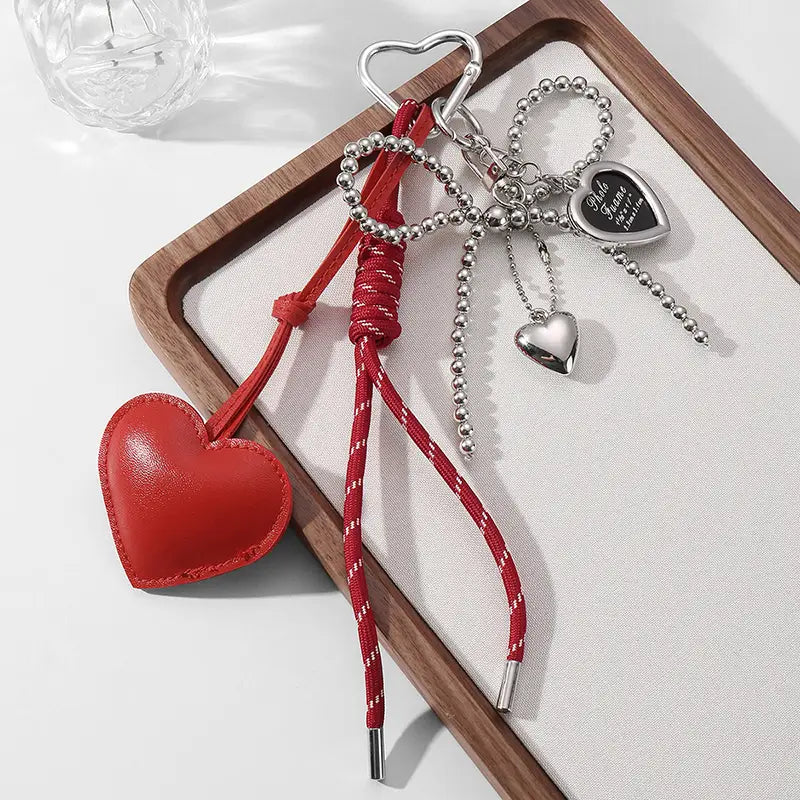 Red heart-shaped leather keychain with braided red cord and silver metal accents for bag decoration.