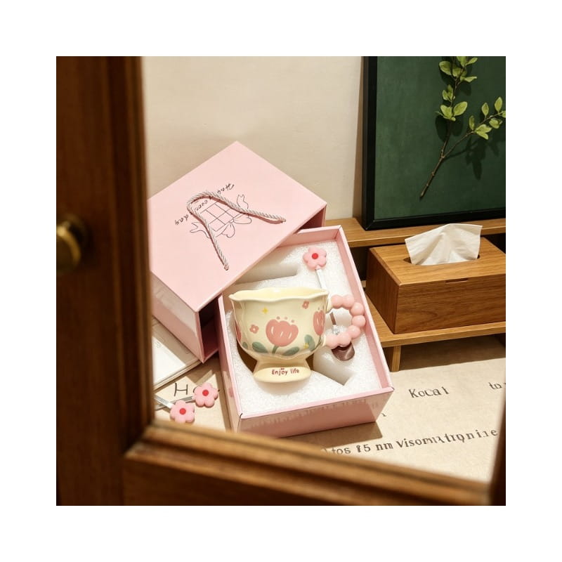 Une tasse tulipe en céramique rose pastel, avec un motif floral et une anse assortie en perles roses, placée dans une boîte cadeau coordonnée.
