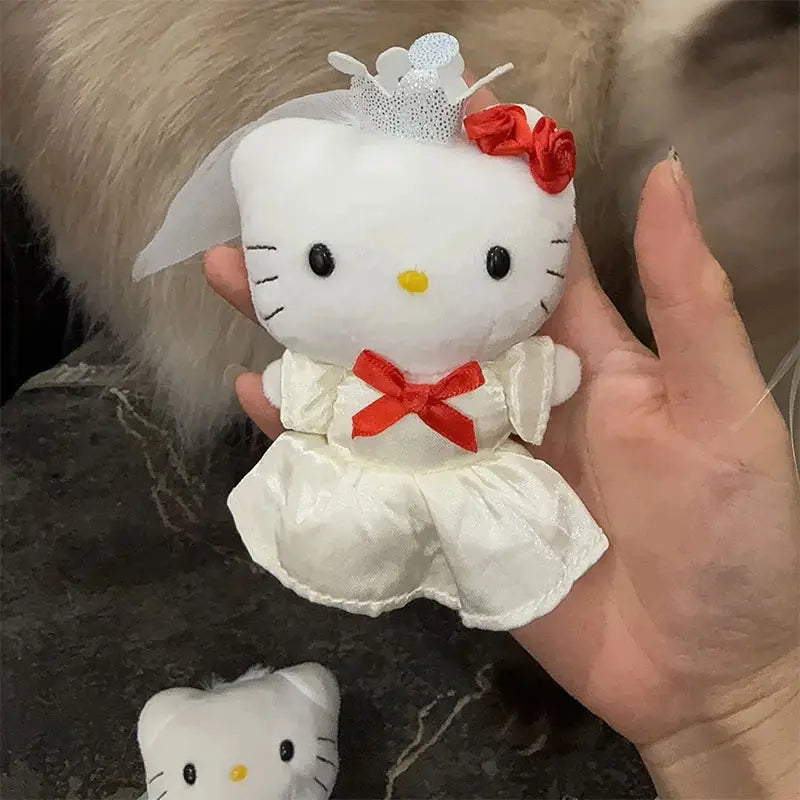 Porte-clés en peluche Hello Kitty blanche, habillé d’une robe de mariage en satin avec des accents de ruban rouge et un voile en dentelle.