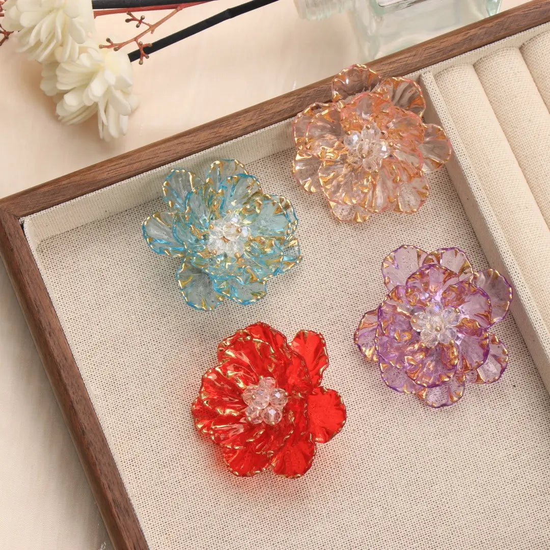 Broche en forme de fleur de cristal, accessoire de mode, présentant quatre fleurs en verre colorées, avec des pétales bordés d’or et des centres en cristal transparent.