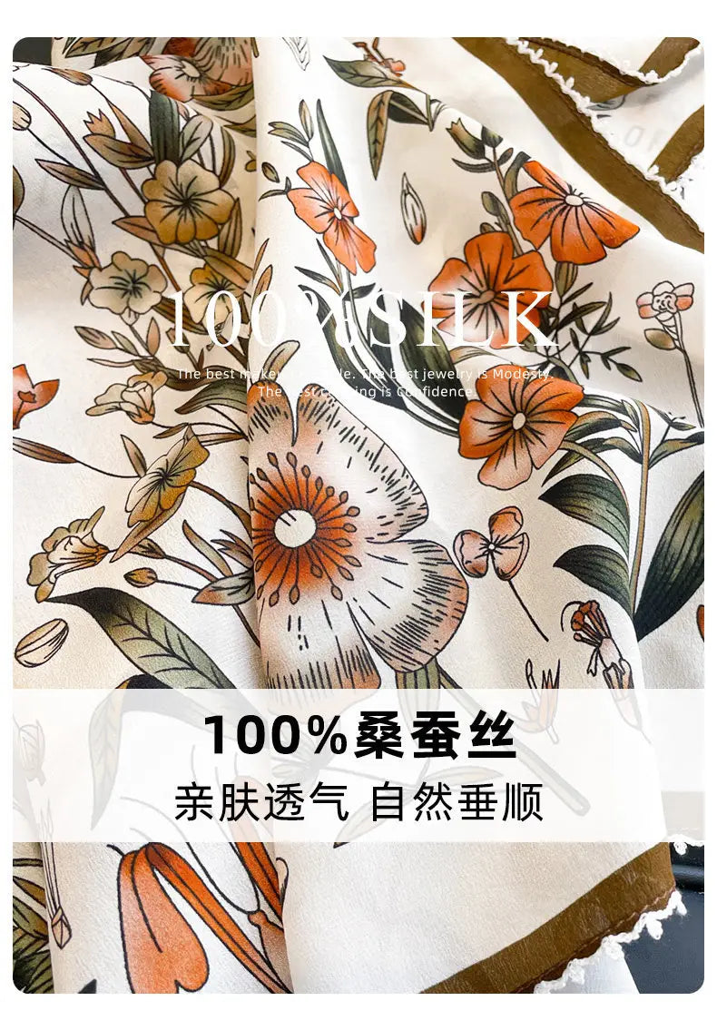 A delicate cream-colored silk floral square scarf features a vibrant pattern with orange brown and green blossoms and leaves.
