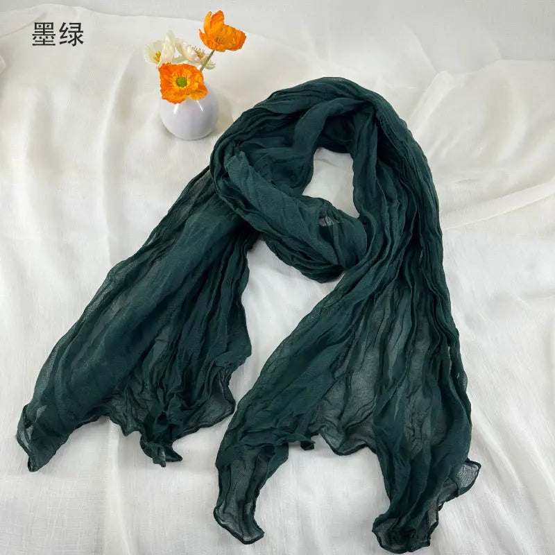 Écharpe en coton et lin plissé en mousseline de chiffon vert foncé, avec une texture translucide douce et des bords volantés délicats.