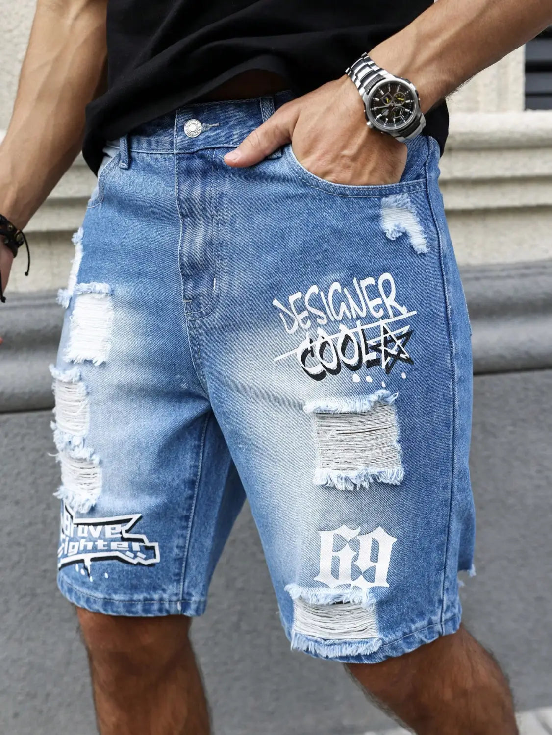Shorts en jean déchirés pour hommes, de couleur bleue, avec des patchs abîmés, des textes et graphismes style graffiti blanc, y compris « designer cooler » et « 69 », avec des bords effilochés, pour un look streetwear décontracté.