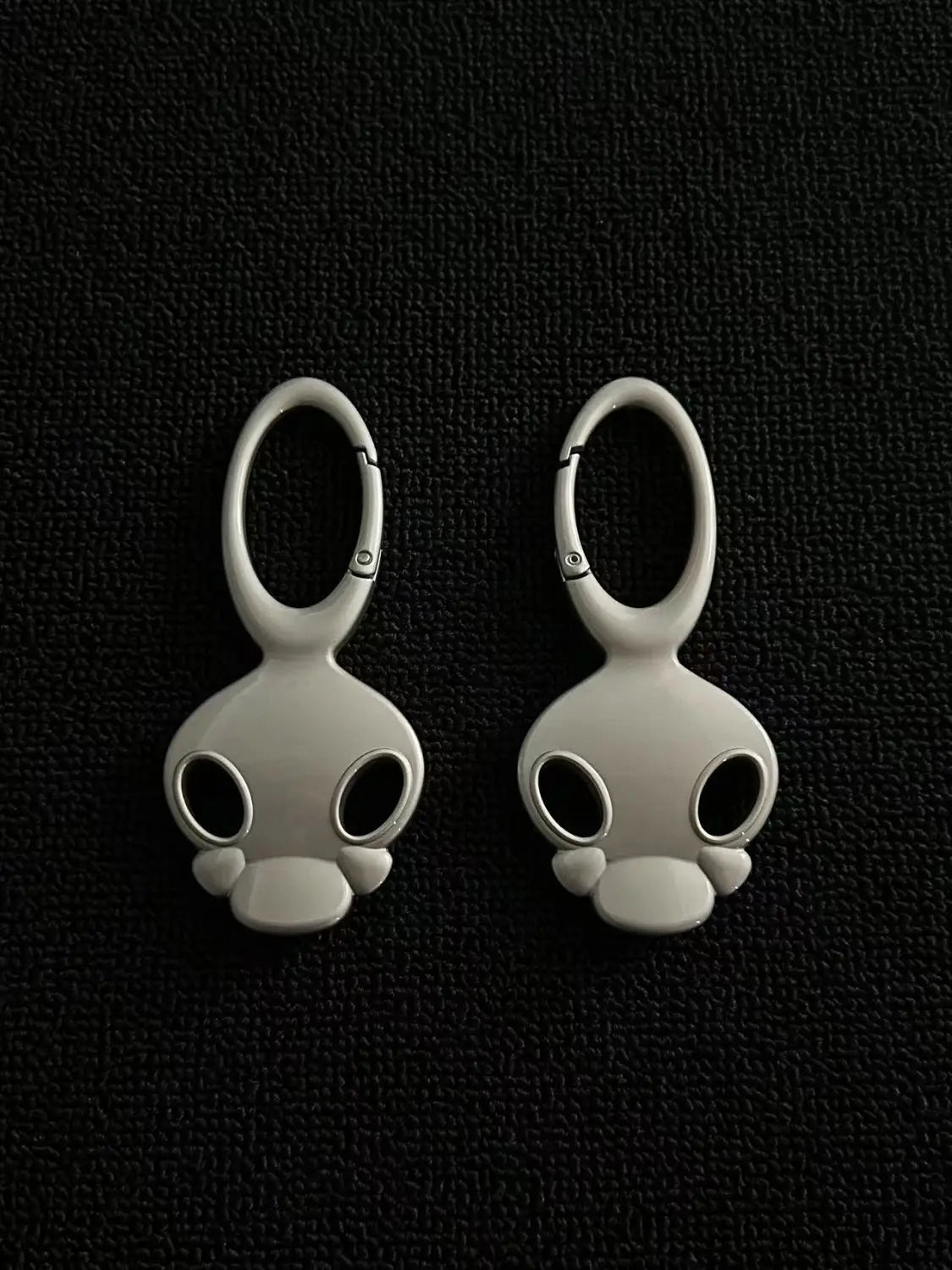 White enamel skull-shaped car keychain with a metallic loop and snap closure for use as a bag charm.