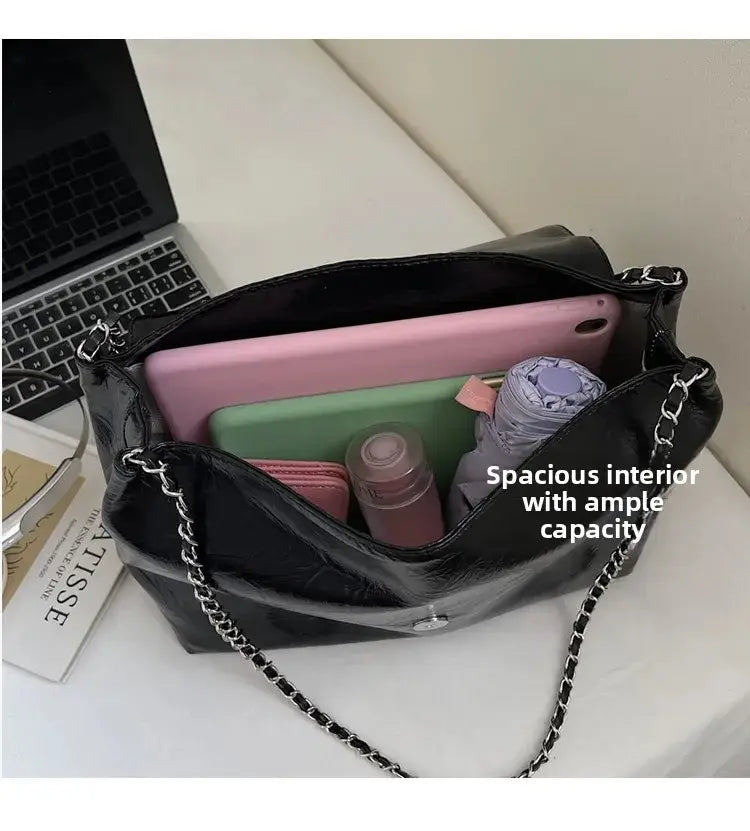 Bolso bandolera negro de charol con correa de cadena plateada y cierre con solapa frontal, diseño de gran capacidad para un uso versátil