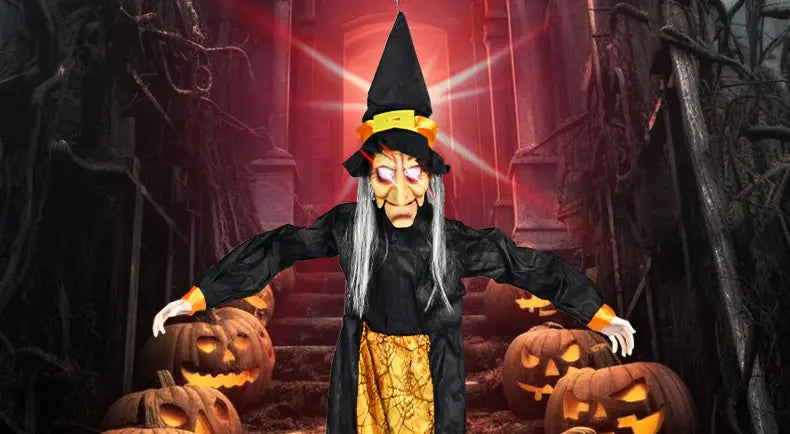 une figurine animée de sorcière d’Halloween suspendue, en noir et jaune, avec un chapeau pointu, de longs cheveux gris, des yeux rouges lumineux et des mains gantées orange, est présentée entourée de citrouilles sculptées, idéale pour une maison hantée ou une collection d’accessoires de jouets électriques hantés.