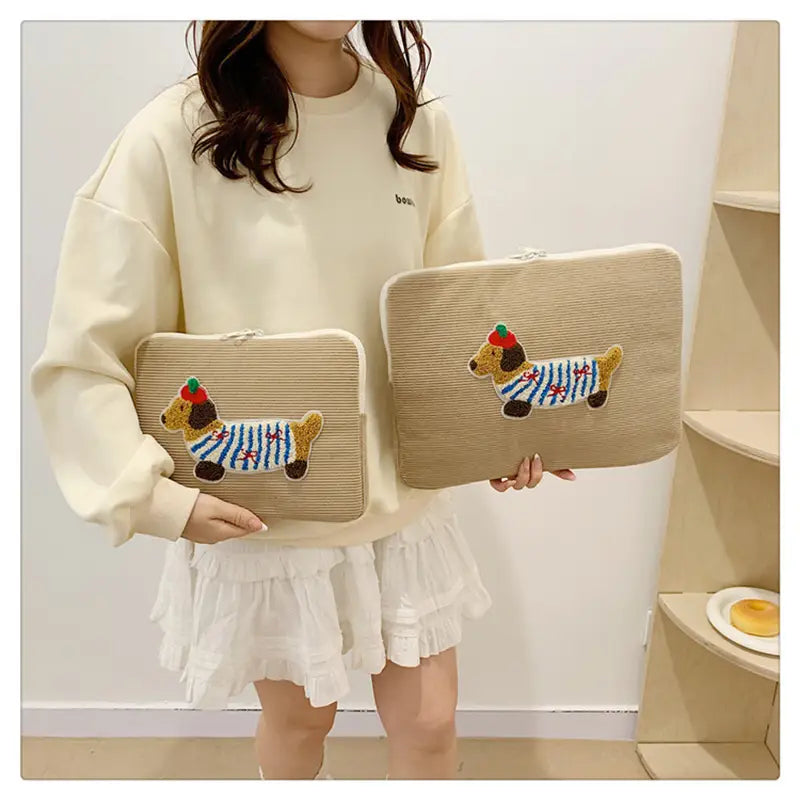 Beige Kord-Laptophülle für MacBook Pro mit einer bestickten Dackel-Figur in einem gestreiften Pullover und roter Mütze.