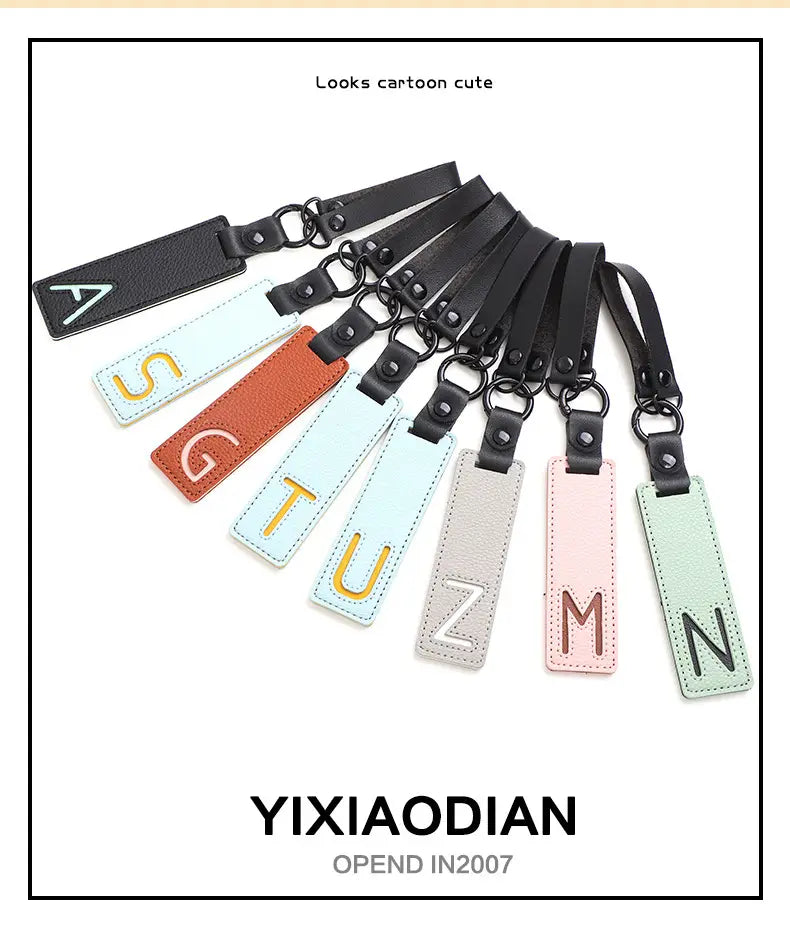 Pastel-colored leather letter keychain alphabet pendants with black straps and metal rings featuring embroidered initials in gold or brown thread ideal for party gifts.