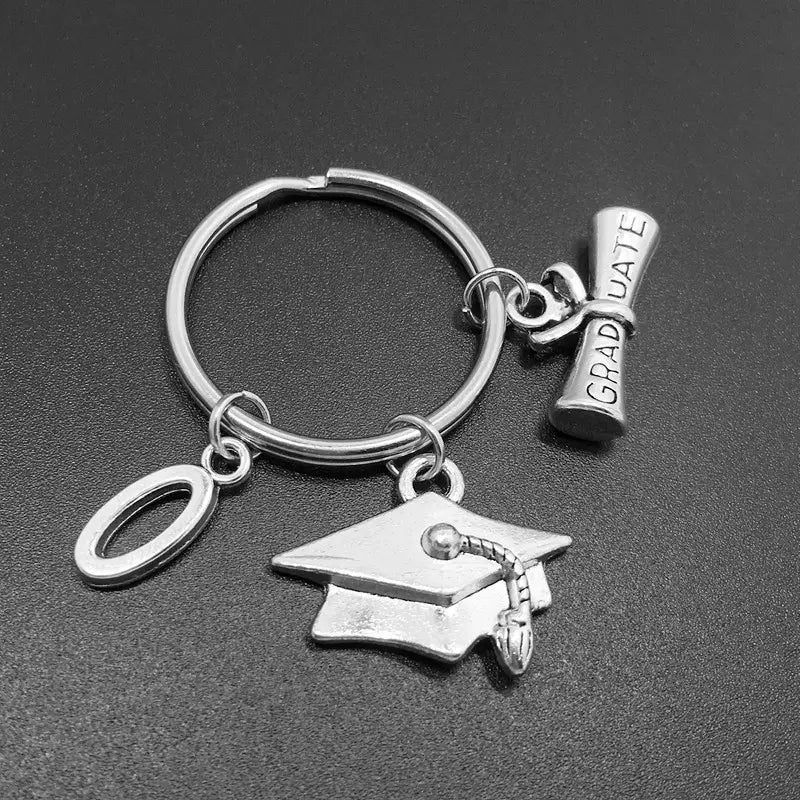Silberner Schlüsselanhänger zur Abschlussfeier mit einem Anhänger in Form des Buchstabens O aus Silber, einem Anhänger mit Tasse und Quaste sowie einem mit Graduate gravierten Diplom-Anhänger.