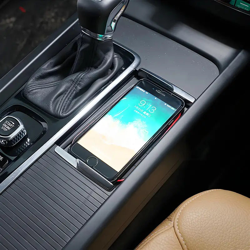 black smartphone with glossy screen displaying teal and white wallpaper resting in sleek black wireless car charger tray for volvo xc90 xc60 v60 and s90 models