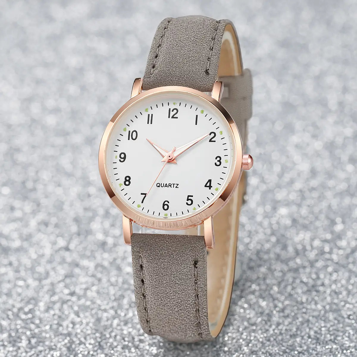 A delicate arabic dial rose gold women’s watch with a white dial and gray suede leather strap.