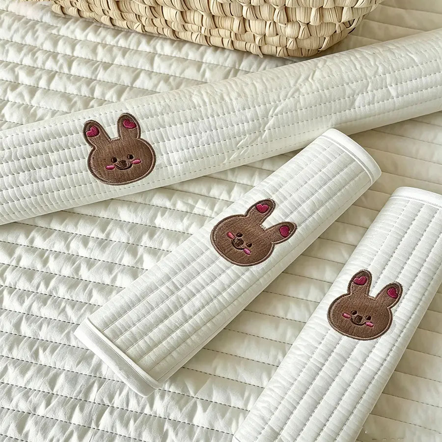 ベビーカー用アクセサリーセットの刺繍入りベアカバーより。かわいらしい茶色の刺繍入りウサギの顔と、耳にピンクのハートをあしらった白いキルティングのカーシートベルトプロテクター。