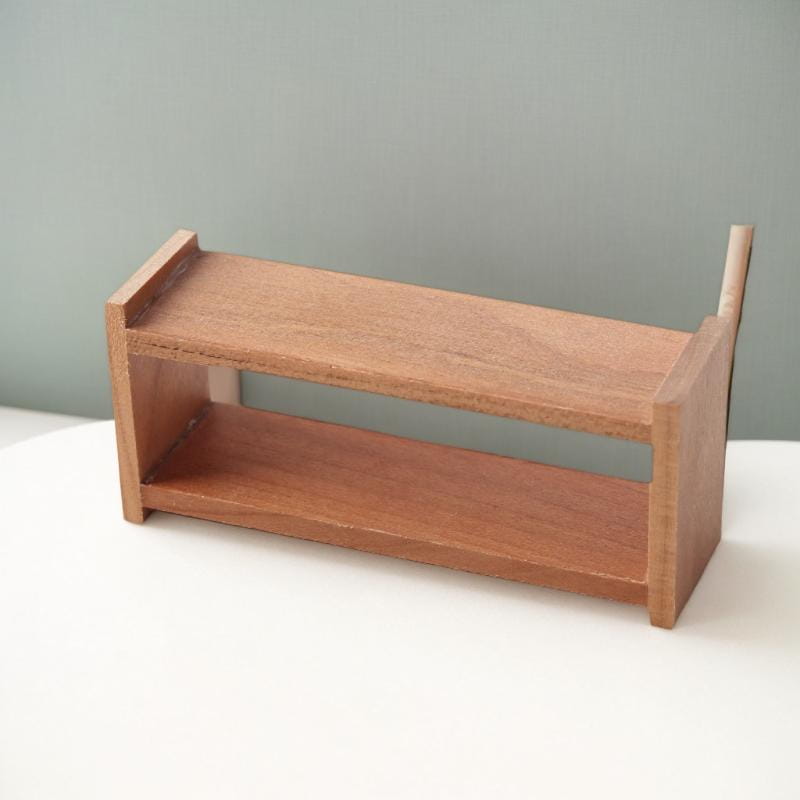 Ein minimalistisches zweistufiges Holzregal mit warmem natürlichem Finish und klaren Linien, entworfen als Miniaturmöbel für Puppenhäuser.