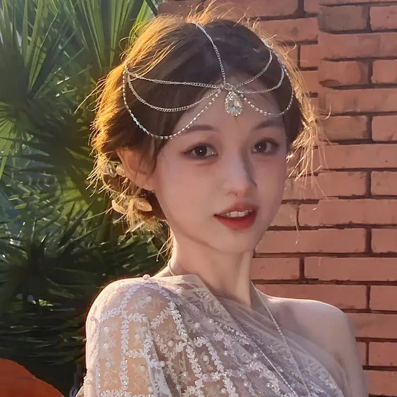 赤い宝石のゴールド前髪チェーンヘアペンダントコレクションにおける、きらめくラインストーンと中央の雫のような形のクリスタルで飾られたシルバーチェーンの前髪ヘッドピース。髪の装飾として優雅にお使いいただけます。