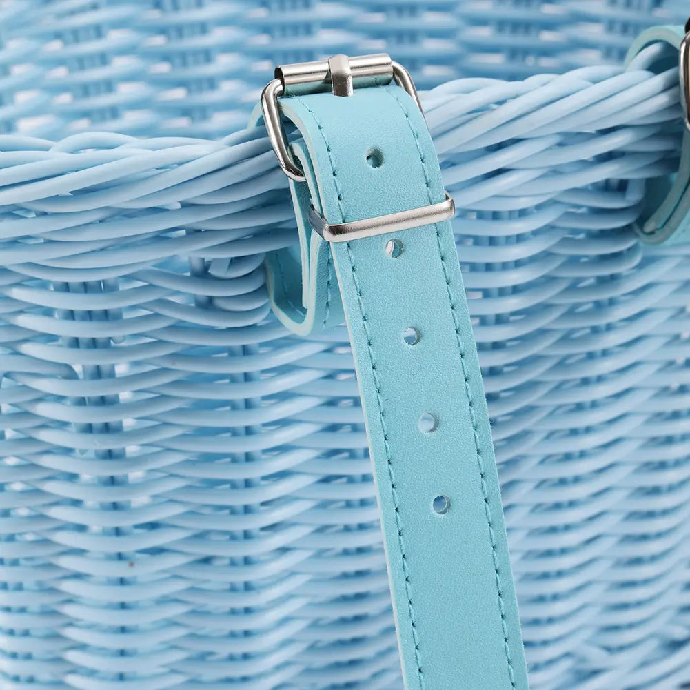 Light blue leather strap with silver-toned metal buckle attached to a woven wicker kids woven bicycle basket set with bell and tassels.